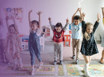 Early childhood students in a classroom dancing with their arms up